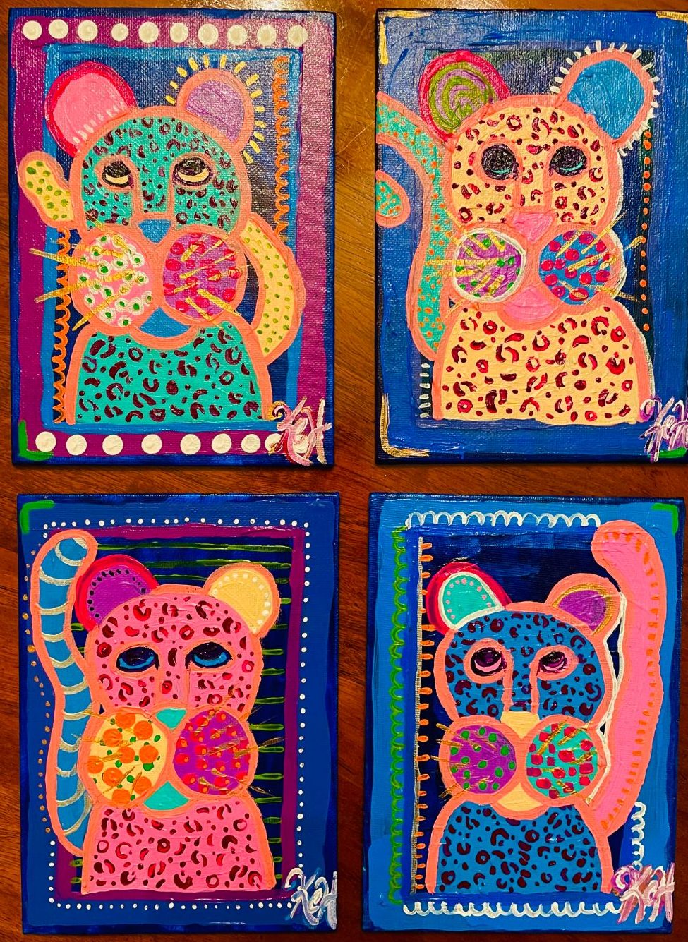 Four small paintings of spotted cats in pink, teal, peach and blue