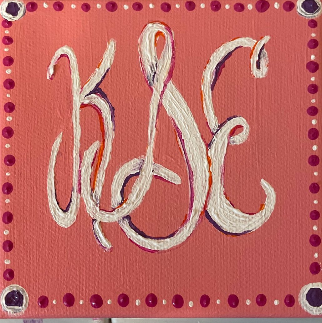 Small painting of a white monogram on coral with a dotted border